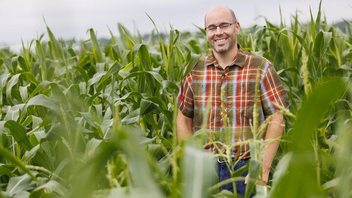 Dr. James Schnable standing in a corn field smiling.